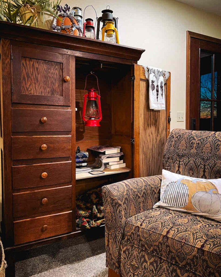 wooden wardrobe with two doors and five draws next to wingback chair.
