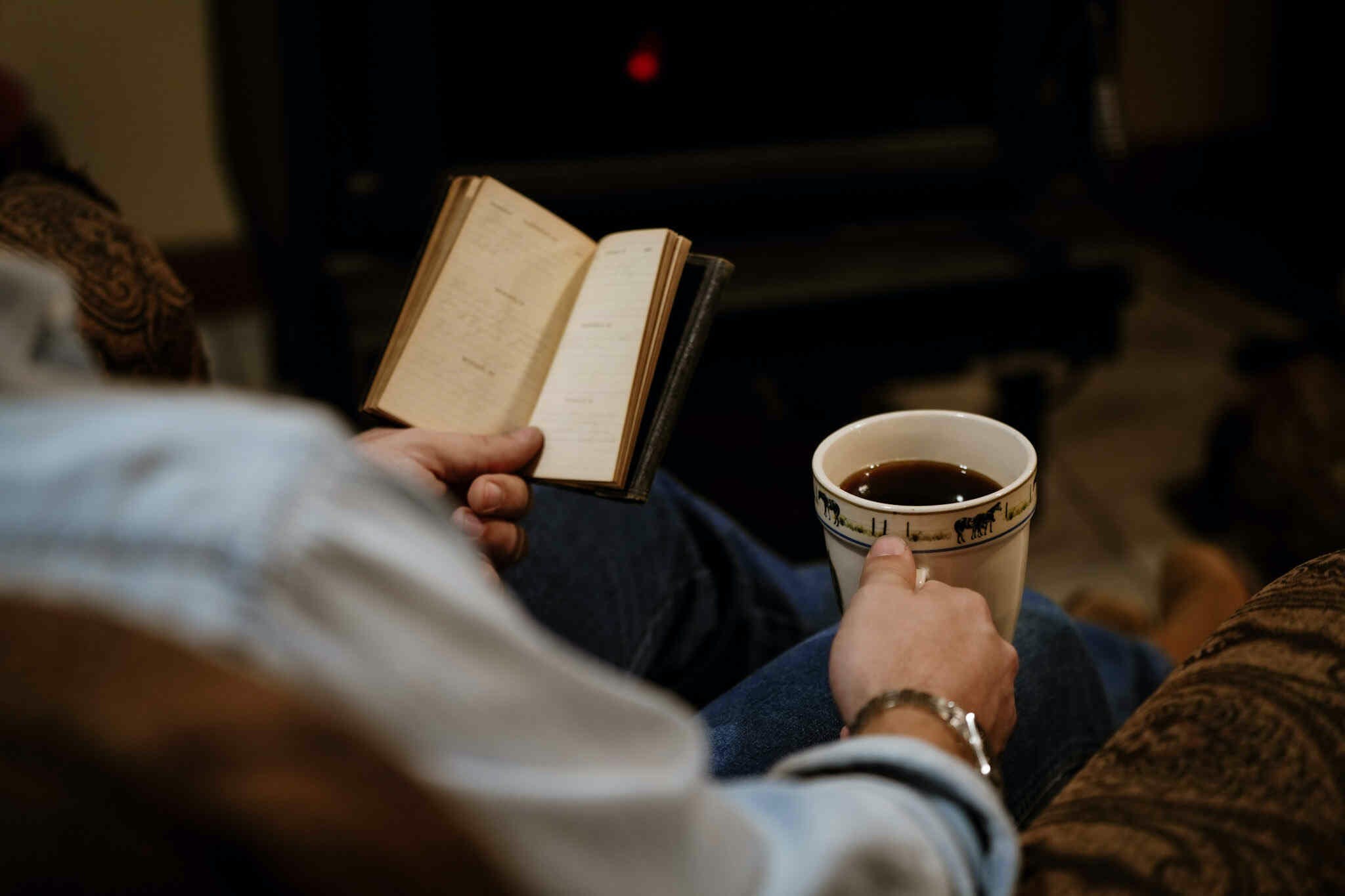 C.E. Robertson sitting in the hearth room in front of the wood burning stove with a cup of coffee in one hand and diary of his great great great grandfather in the other.