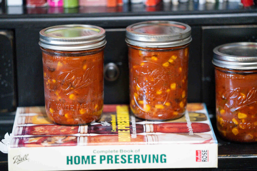 Two pint canning jars with black bean and corn salsa in them. Sitting on a home preserving book.