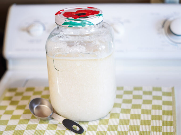 gallon glass jug of homemade laundry detergent and measuring spoon on washing machine