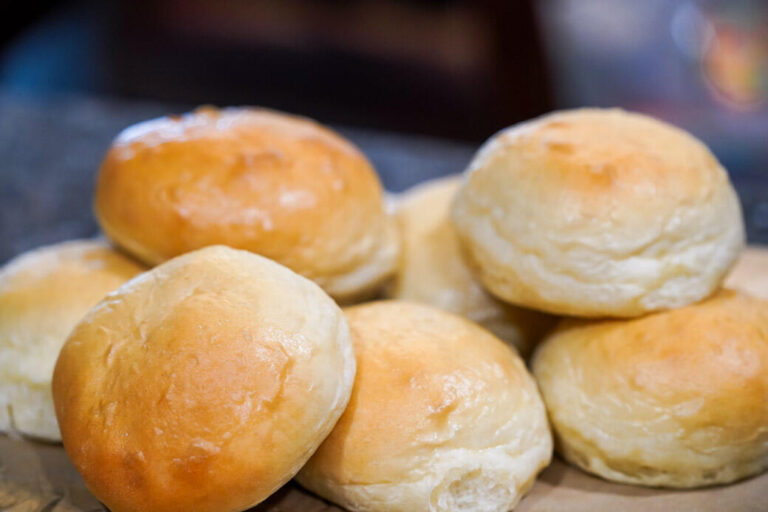 several golden-brown homemade sourdough hamburger buns in a pile on counter