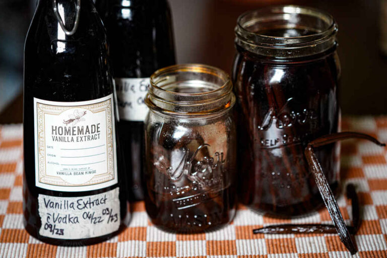 glass bottles and mason jars of homemade vanilla extract on orange and cream checkered placemat